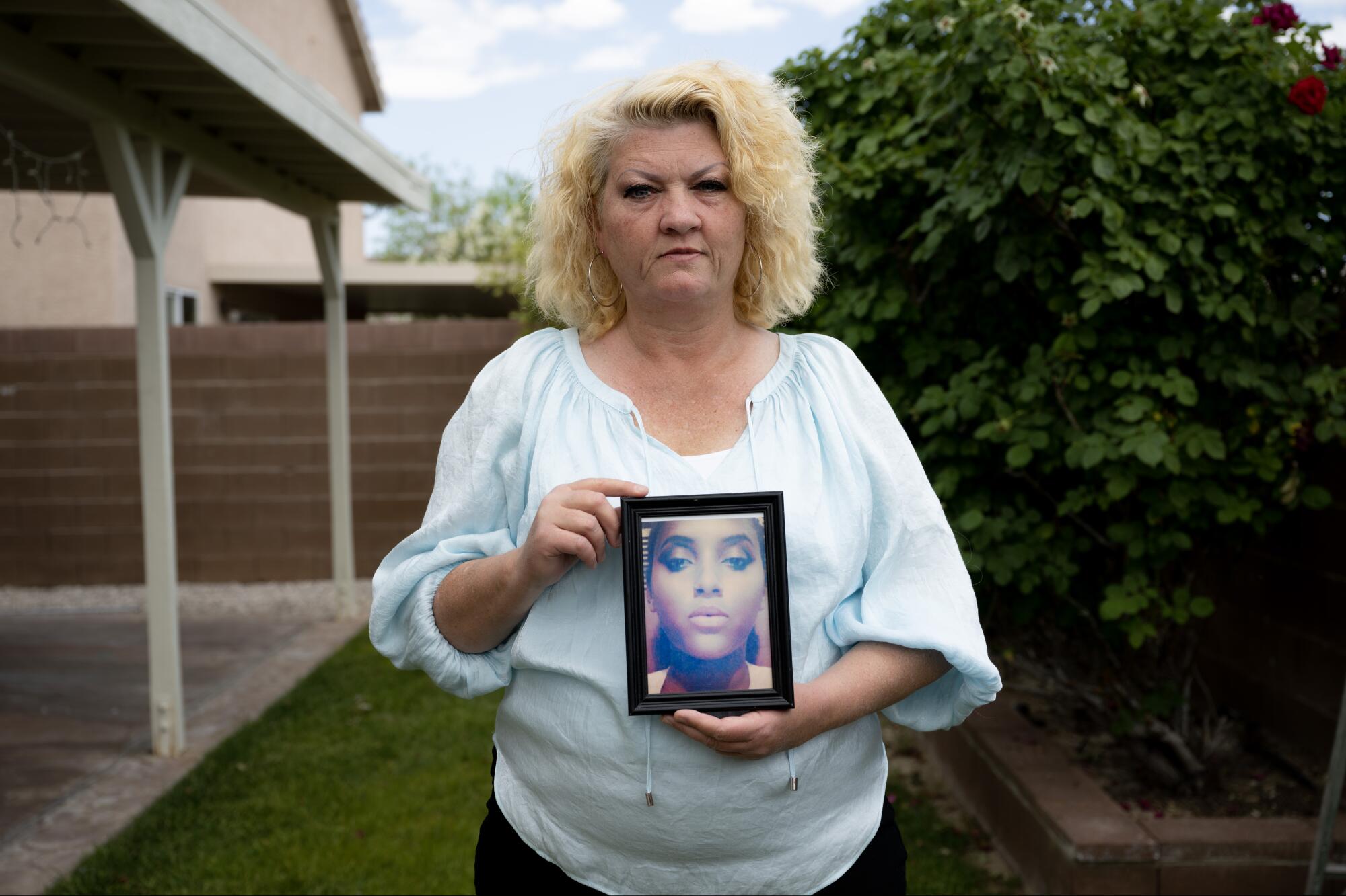 A woman in the backyard of a home holds a photgraph.