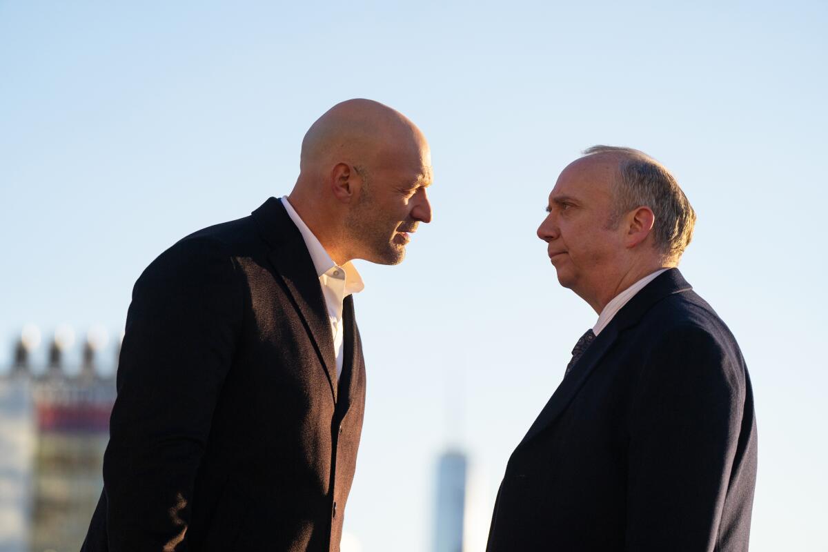 Two men in suits stare each other down on a New York rooftop