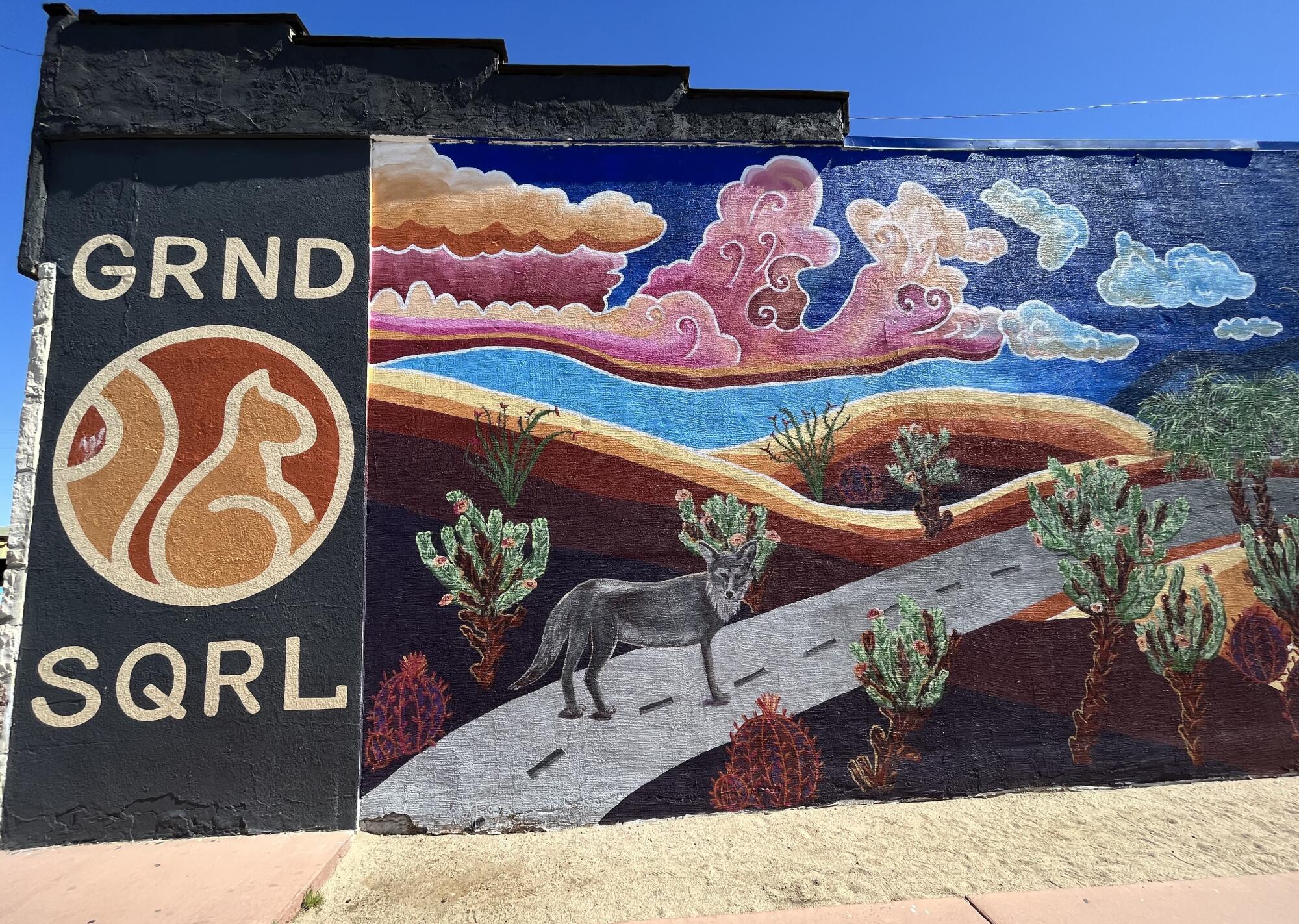 A mural depicts a three legged coyote standing on a road in the desert. 