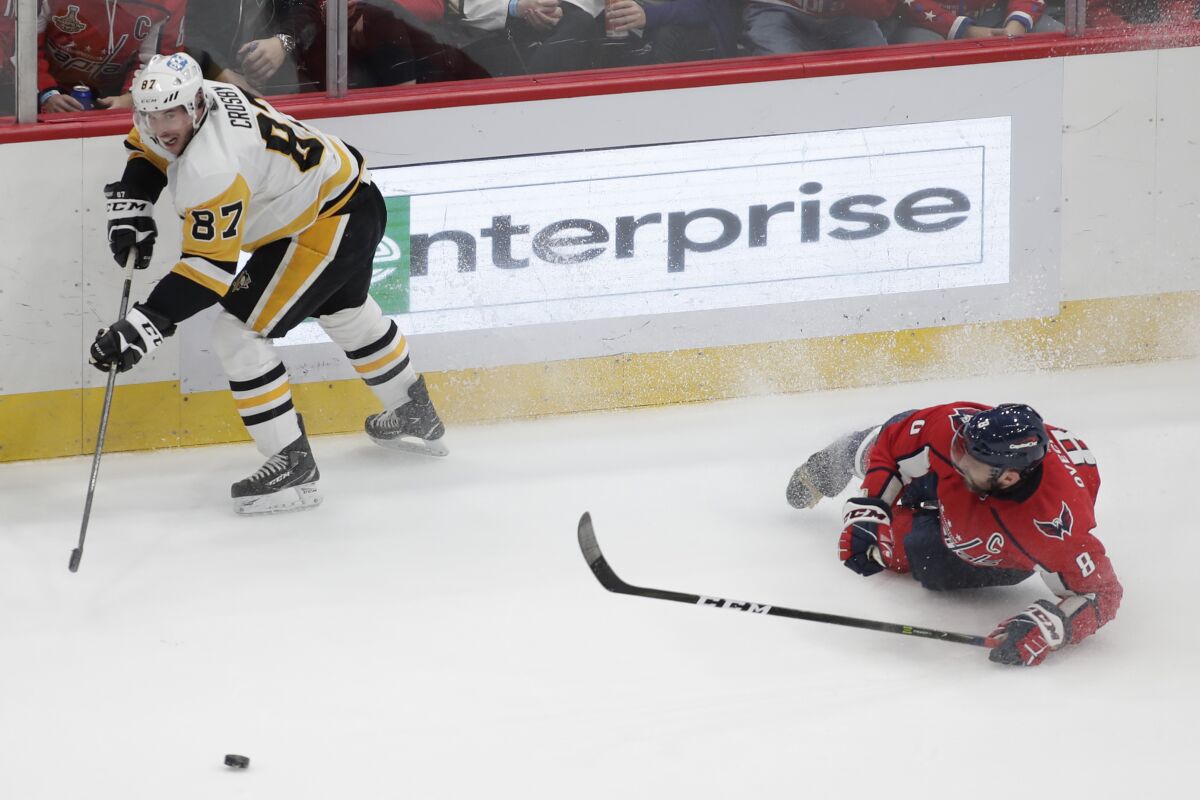 Pittsburgh Penguins' Sidney Crosby (87) passes the puck as Washington Capitals' Alex Ovechkin (8) falls during the third period of an NHL hockey game, Friday, Dec. 10, 2021, in Washington. (AP Photo/Luis M. Alvarez)