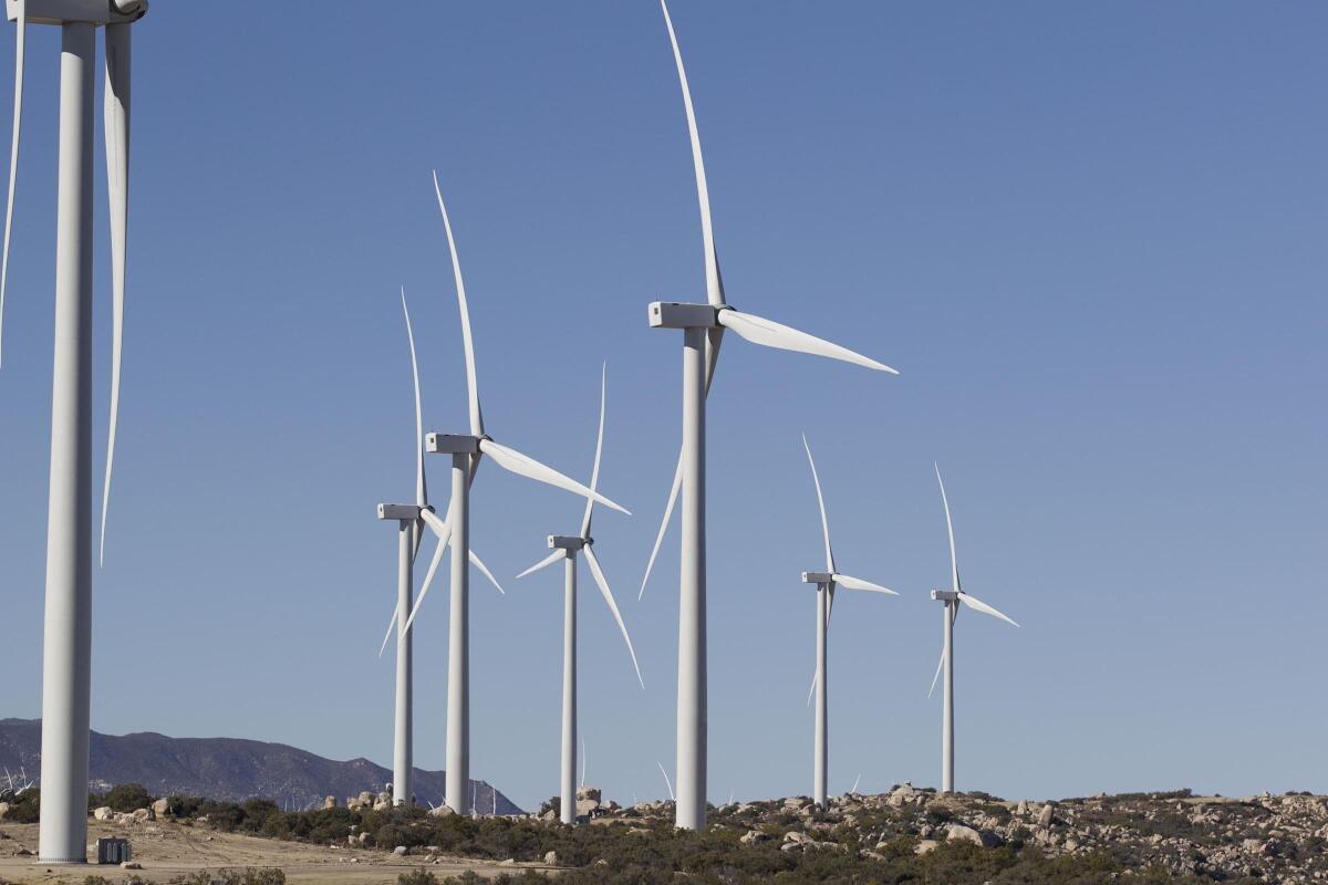 White windmills stand amid a rocky landscape, with mountains in the background