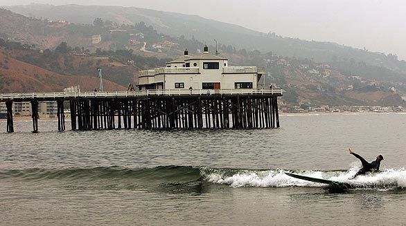 A surfer falls off his board Thursday while catching a wave near the Malibu Pier. Restoration of the pier is still in progress, but one of the four planned restaurants, The Malibu Pier Club, is already open. The two historic 1940s buildings seen at the end of the pier will house Ruby's Shake Shack and a sport-fishing retail shop, scheduled to open in August. A surf museum is being added on the second floor of one of the buildings.