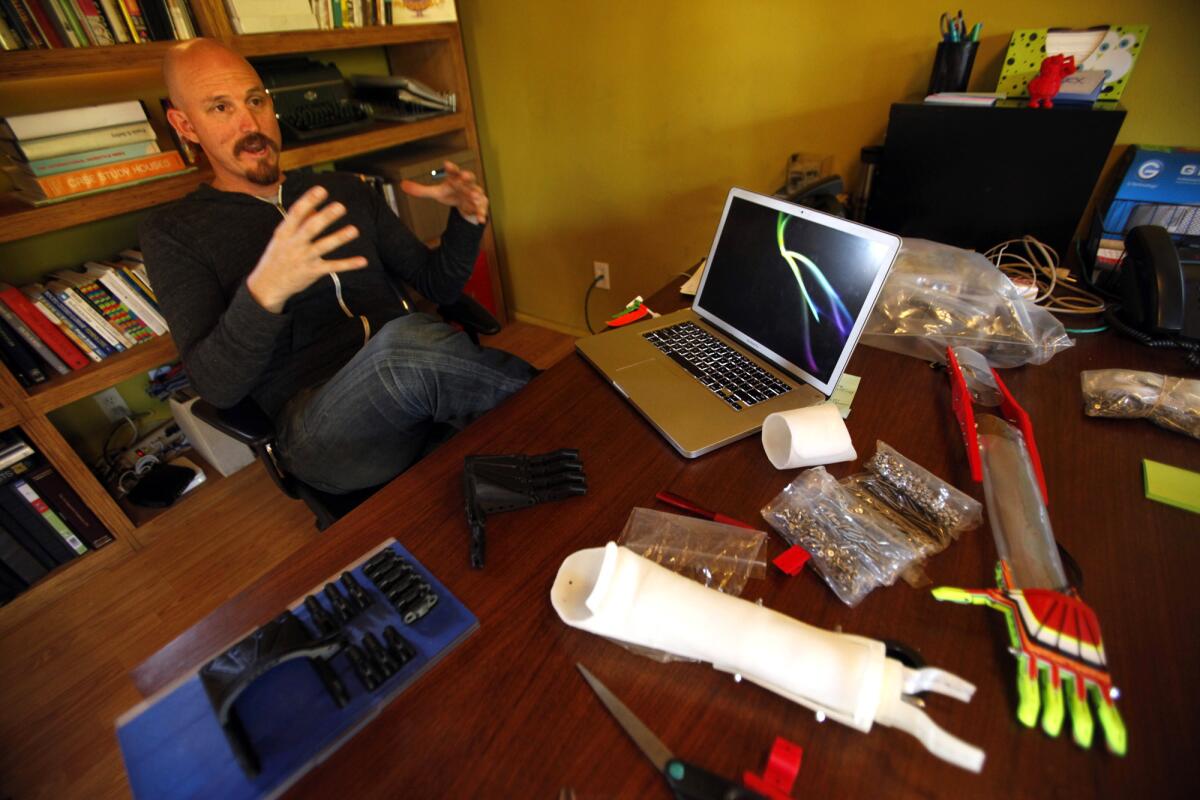 Mick Ebeling, founder and chief executive of Not Impossible, at his desk with prosthetic arms and hands that he created with his 3-D printer at his office in Venice. Ebeling is the unlikely leader of a team dedicated to tackling the physical limitations that arise from conditions such as blindness and paralysis.