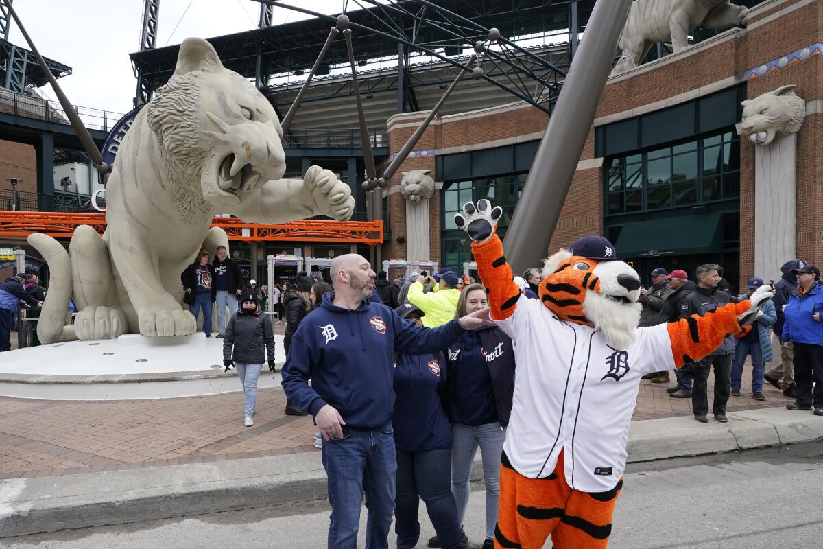Paws, the Detroit Tigers mascot, photobombs a group in front of the Tigers statue outside Comerica Park