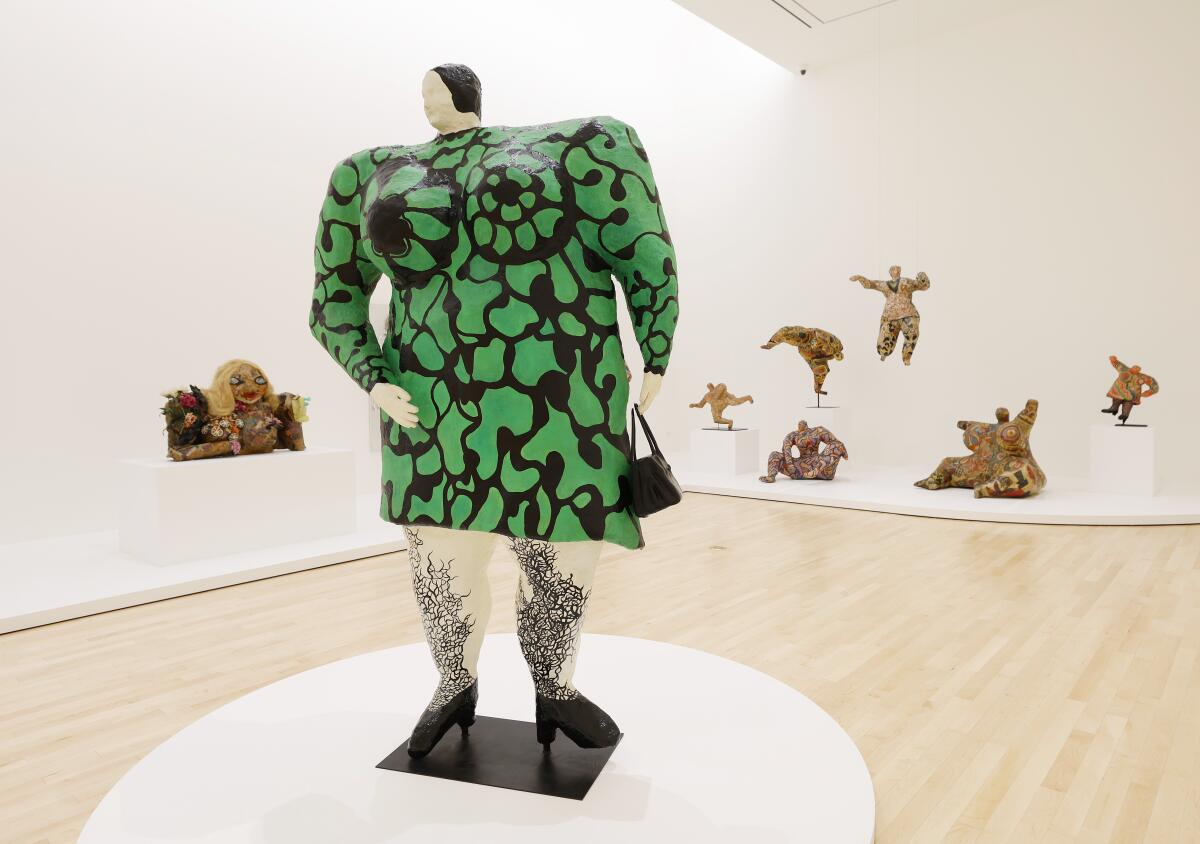 A sculpture of a woman in a green and black dress, with other sculptures in the background, in a museum.
