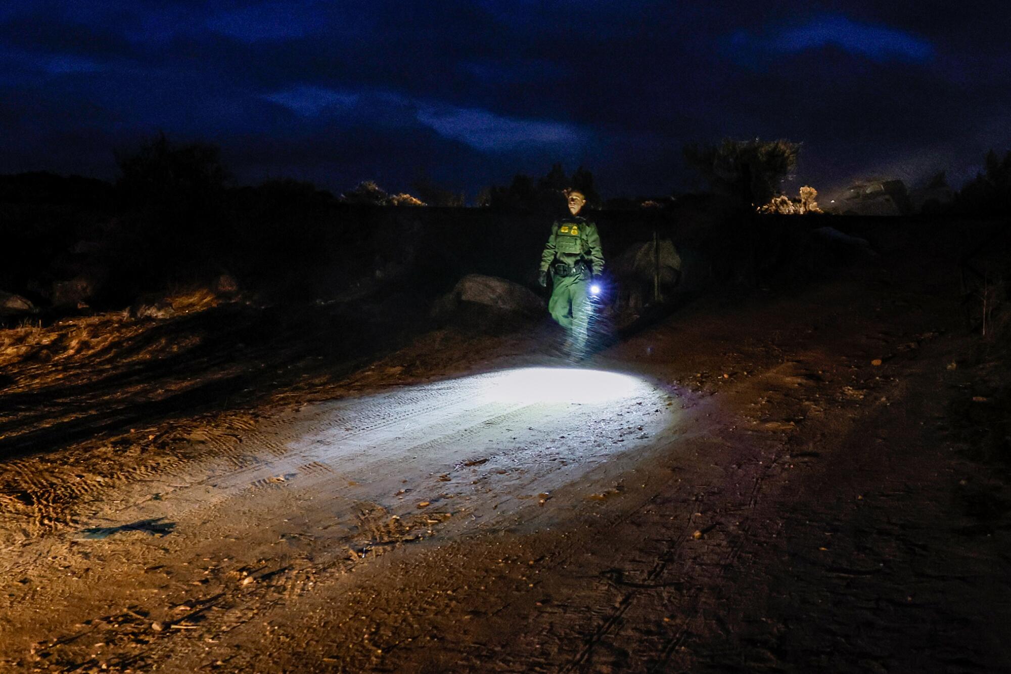 A Border Patrol agent walks with a flashlight.  