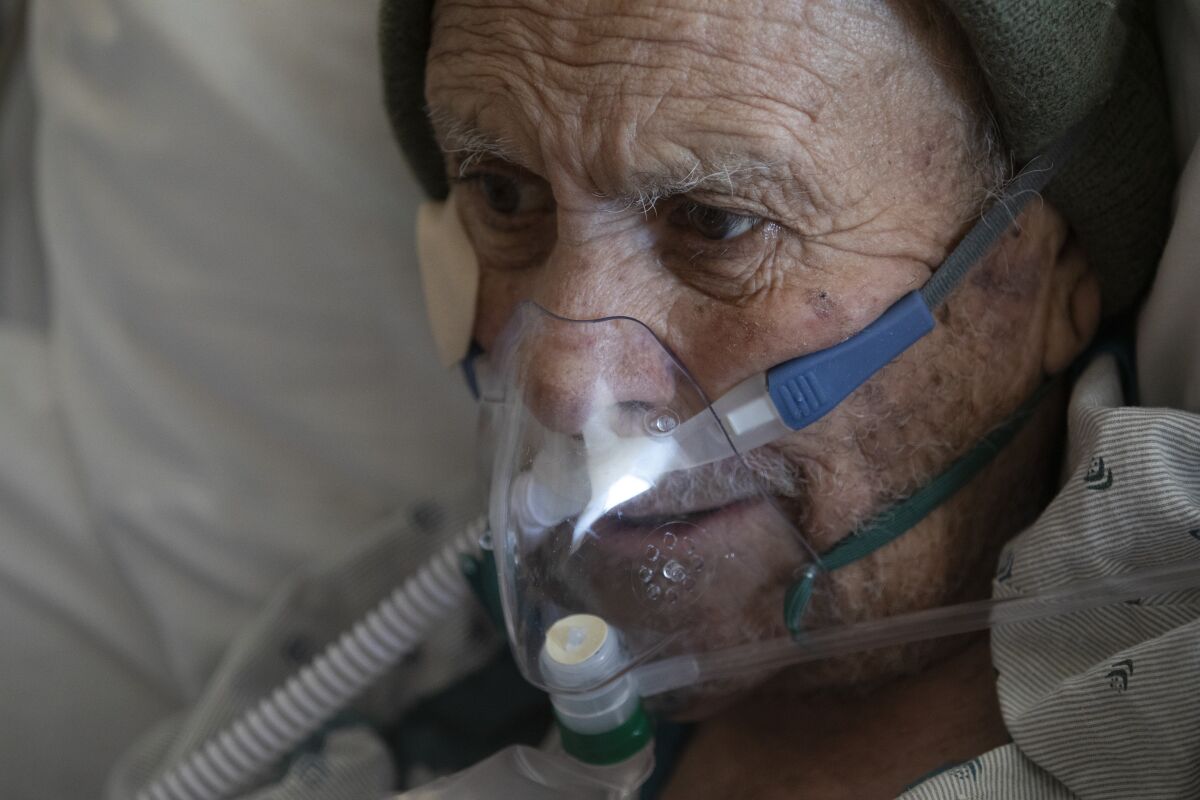 A man wears an oxygen mask connected to a tube while in bed.