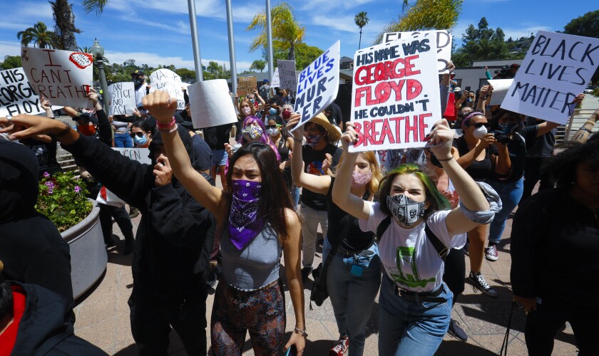 Protesters hold signs including "His name was George Floyd. He couldn't breathe" and "Black lives matter."