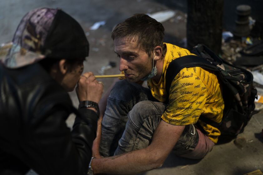 Homeless addicts Brandice Josey, left, uses a straw to blow a puff of fentanyl smoke into the mouth of Ryan Smith, who is high on the drug, in Los Angeles, Thursday, Aug. 18, 2022. (AP Photo/Jae C. Hong)