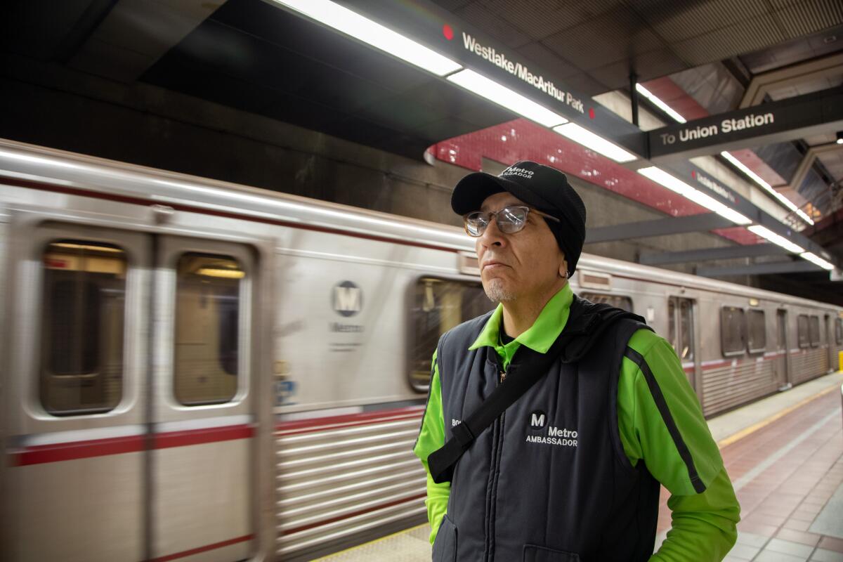 A man in a Metrolink vest and neon shirt walking on a platform as a train blurs past