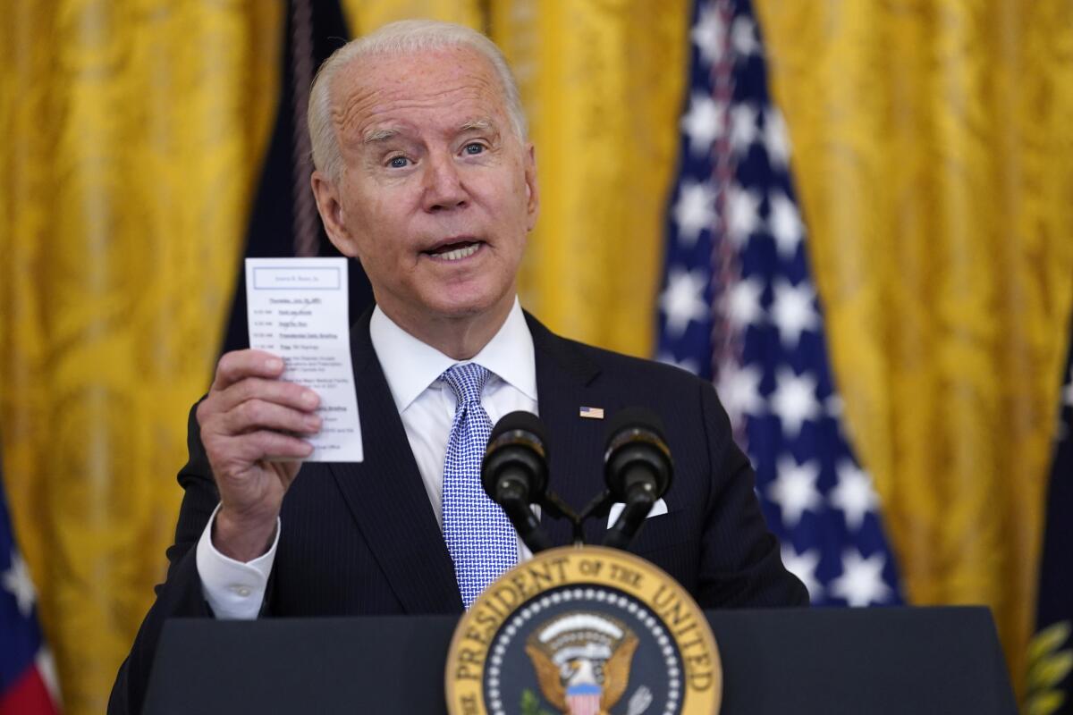 Biden holds up a note card while speaking at a podium at the White House