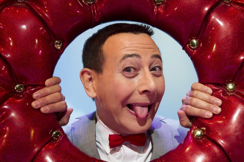 Paul Reubens sticking his tongue out and poking his head through a hole in an upholstered red donut.
