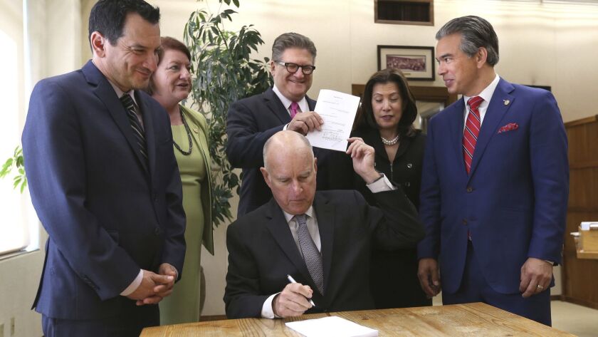 Gov. Jerry Brown hands a copy of a bill to abolish cash bail he signed to state Sen. Bob Hertzberg (D-Van Nuys), who along with Assemblyman Rob Bonta (D-Alameda), right, co-authored the measure, during a ceremony in Sacramento.
