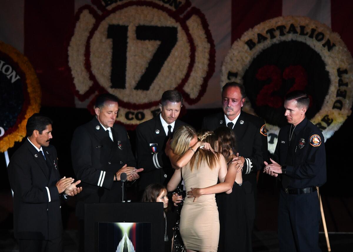 The wife and daughters of fallen L.A. County firefighter Tory Carlon hug during a memorial at the Forum