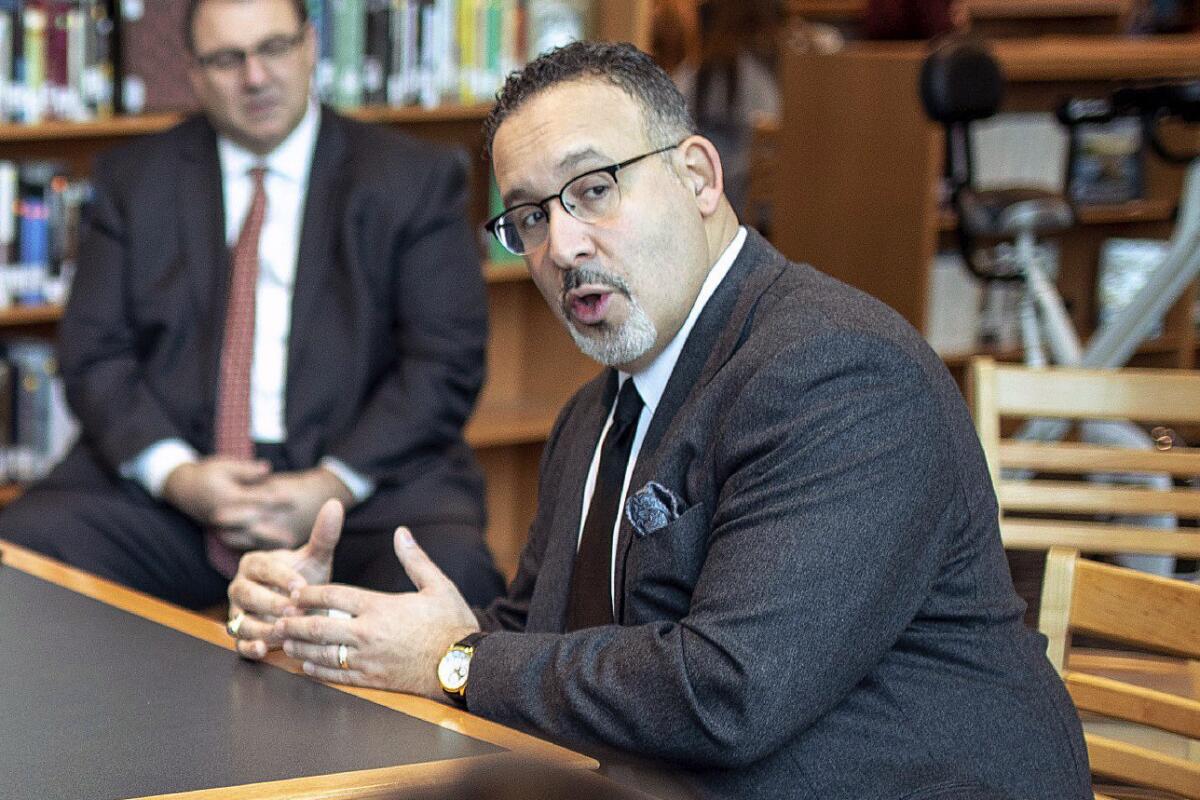 Miguel Cardona, seated at a table, speaks with Berlin High School students in Connecticut.