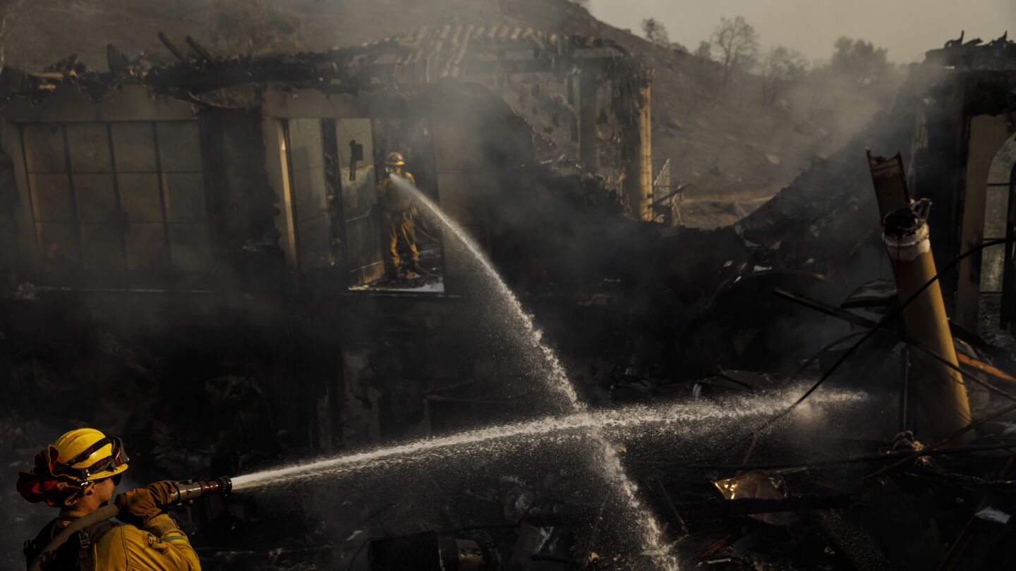 Humboldt County firefighters Lonnie Risling, left, and Jimmy McHaffie, right, spray down smoldering fire underneath the rubble of a home that was destroyed by the Thomas Fire, in Montecito, Calif., Sunday.