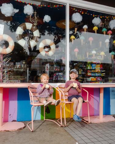 Two children sit eating ice cream outside a colorful storefront