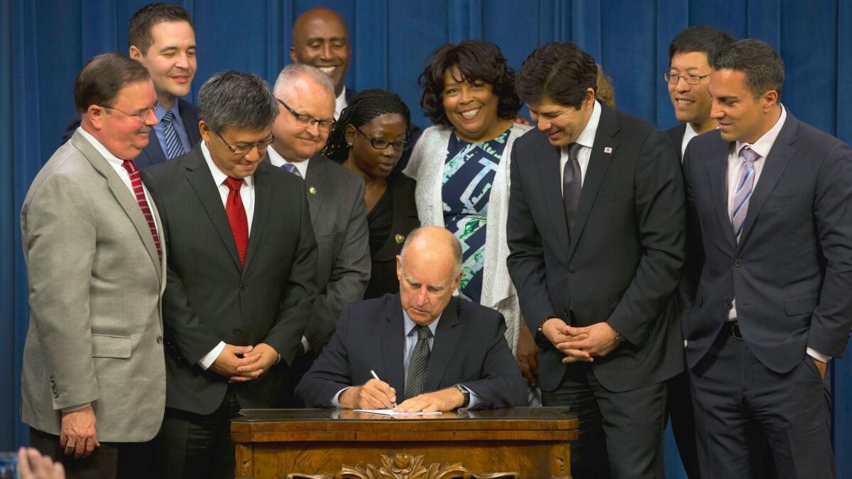 Gov. Jerry Brown signs legislation to automatically enroll millions of private-sector workers in retirement saving accounts as lawmakers and supporters look on at the Capitol in September. The legislation is endangered by opposition from congressional Republicans.