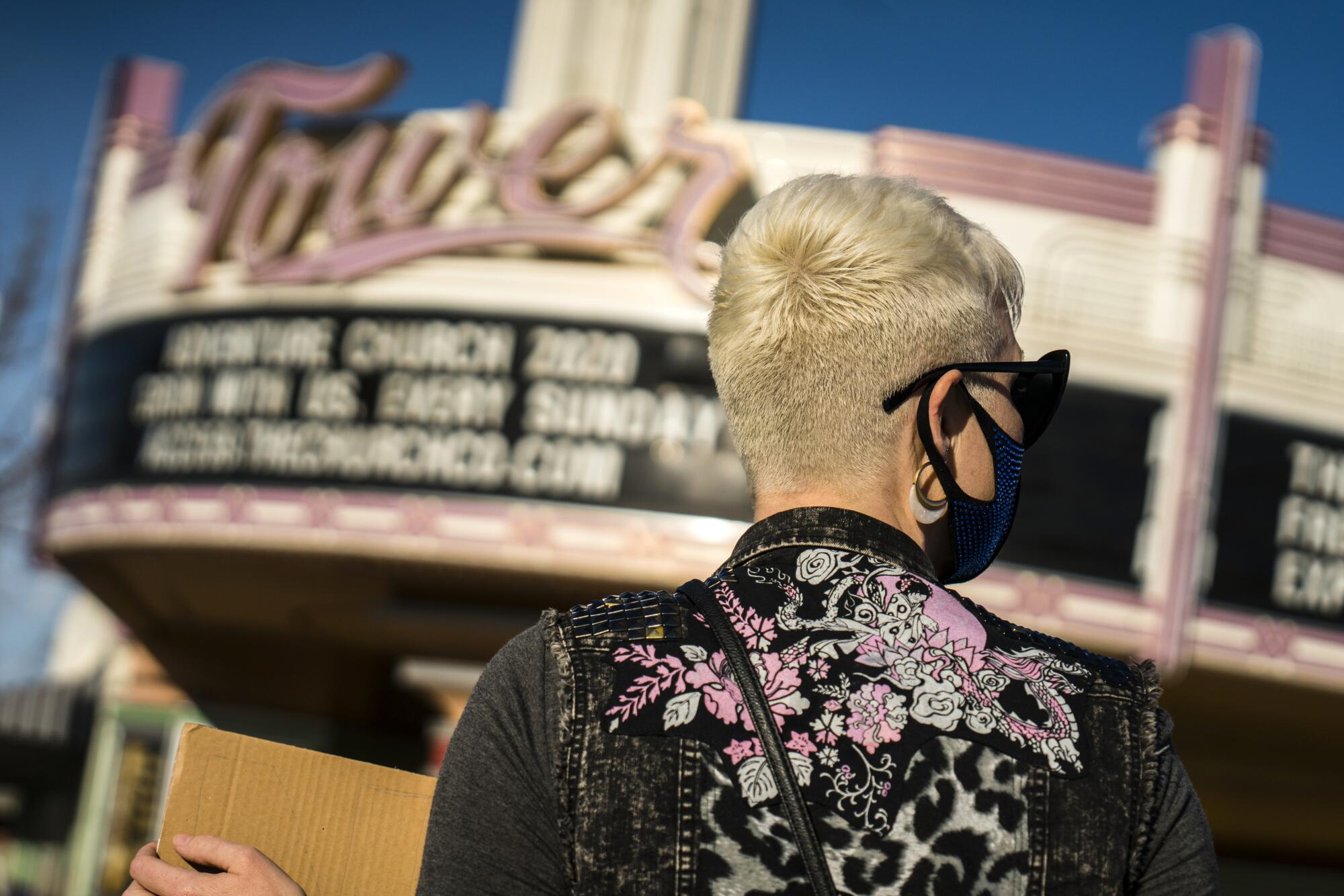 A woman holds a cardboard sign outside an Art Deco theater