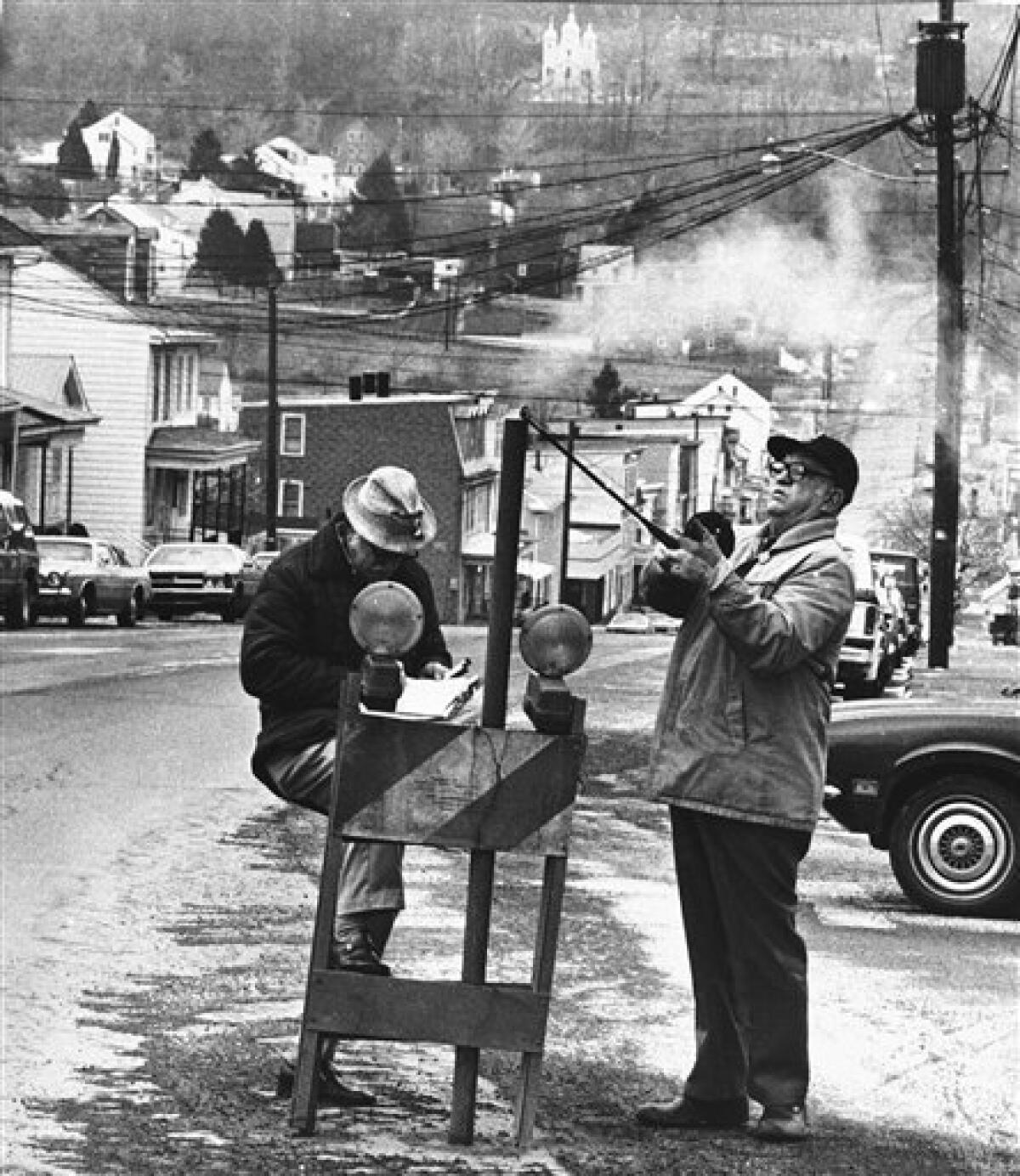 FILE - In this April 1981 file photo, U.S. Bureau of Mines' John Stockalis, right, and Dan Lewis drop a thermometer through a hole on Main Street in Centralia, Pa., to measure the heat from a shaft mine blaze that burns under the town. The few remaining residents of the Pennsylvania coal town decimated by a 48-year-old underground mine fire claim in court papers that a "massive fraud" is being perpetrated against Centralia by parties seeking to grab the mineral rights to hundreds of millions of dollars worth of coal. (AP Photo/Paul Vathis, File)