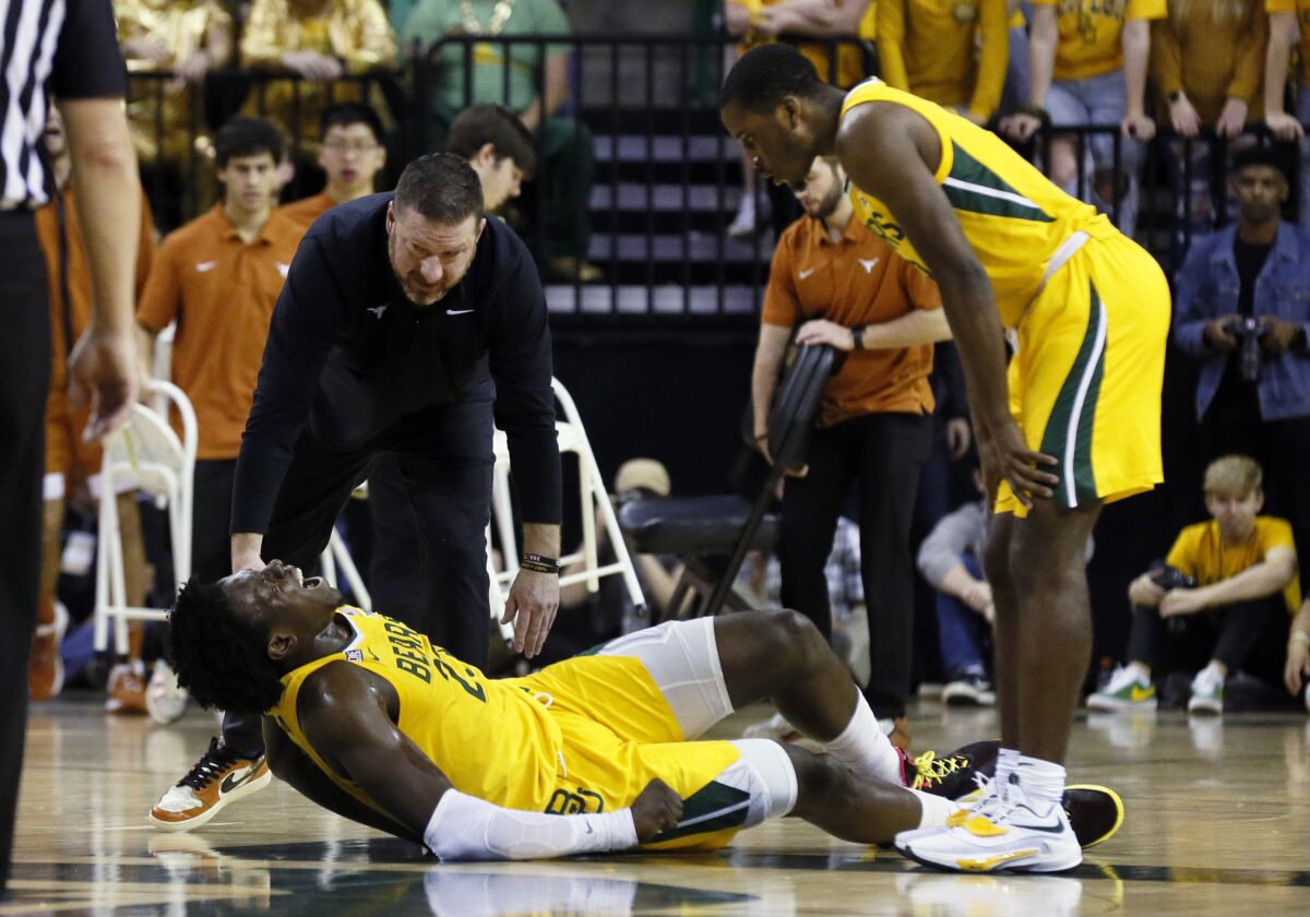 Baylor forward Jonathan Tchamwa Tchatchoua, bottom, is checked on Texas head coach Chris Beard, top left, and Baylor guard Dale Bonner, right after falling to the court with an apparent leg injury during the first half of an NCAA college basketball game on Saturday, Feb. 12, 2022, in Waco, Texas. (AP Photo/Ray Carlin)