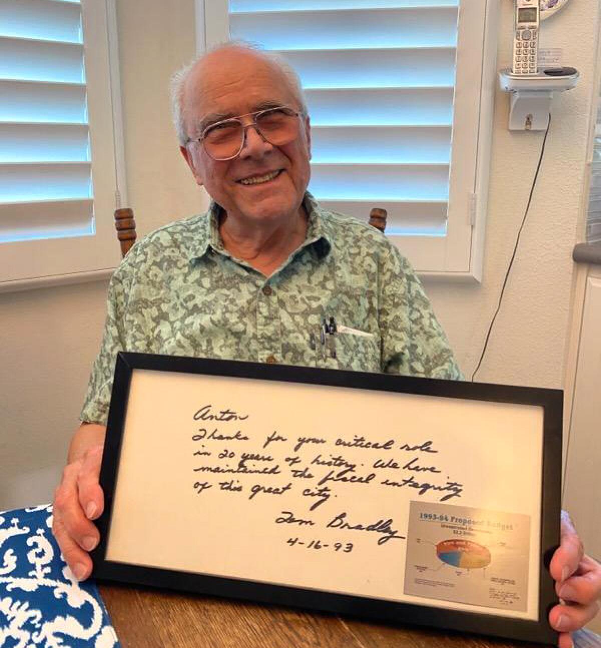 A smiling man holds a framed document signed by Tom Bradley and dated April 16, 1993.