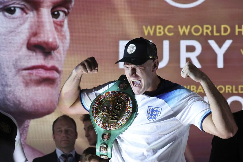 Boxer Tyson Fury the WBC heavyweight champion poses for the cameras with his championship belt and wearing an England soccer shirt after the official weigh-in, in London, Friday Dec. 2, 2022. Tyson Fury will fight against Derek Chisora on Dec. 3, at Tottenham Hotspur's stadium to defend his WBC heavyweight championship. (AP Photo/Ian Walton)