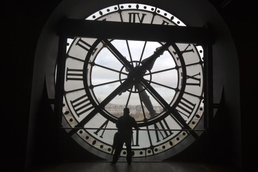 FILE - A visitor looks through the clock of the Orsay museum, overlooking Paris, Oct. 16, 2014. Short-term rental giant Airbnb is listing 11 iconic locations, including the Orsay, for a limited time in a splashy new marketing campaign. (AP Photo/Michel Euler, File)