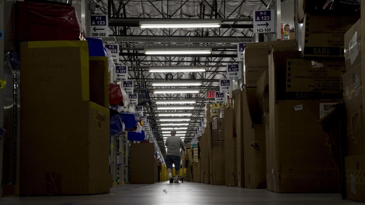 A worker pushes a cart through the rows and rows of merchandise to get items for customers at the Amazon Fulfillment Center in San Bernardino.
