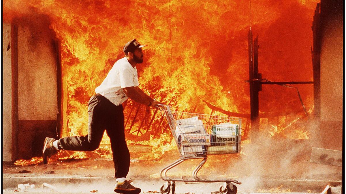 A man with a shopping cart races past a burning shop during the L.A. riots following the Rodney King trial.
