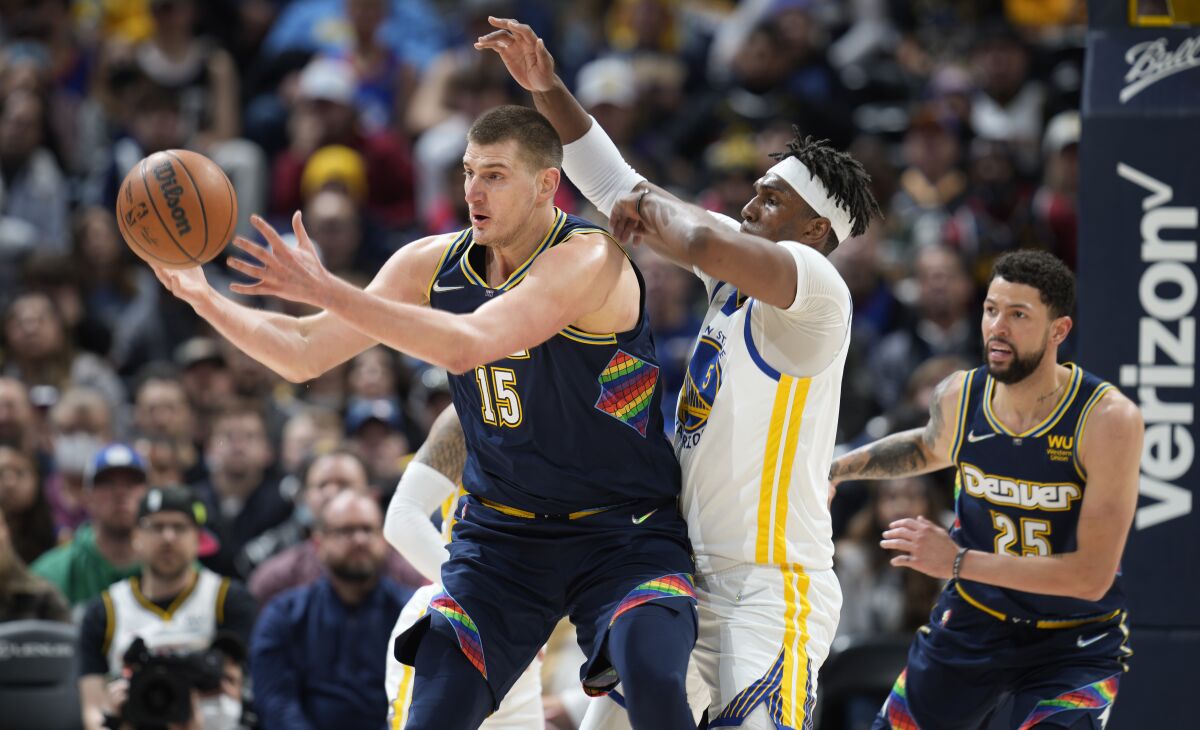 Denver Nuggets center Nikola Jokic, left, fields a pass as Golden State Warriors center Kevon Looney, center, defends while Nuggets guard Austin Rivers looks on in the first half of an NBA basketball game Monday, March 7, 2022, in Denver. (AP Photo/David Zalubowski)