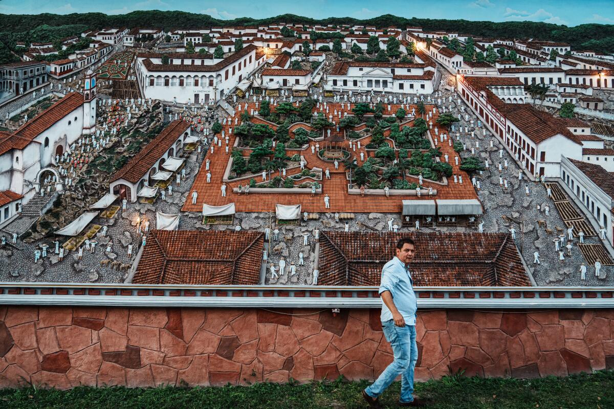 A man stands in front of a mural showing Papantla
