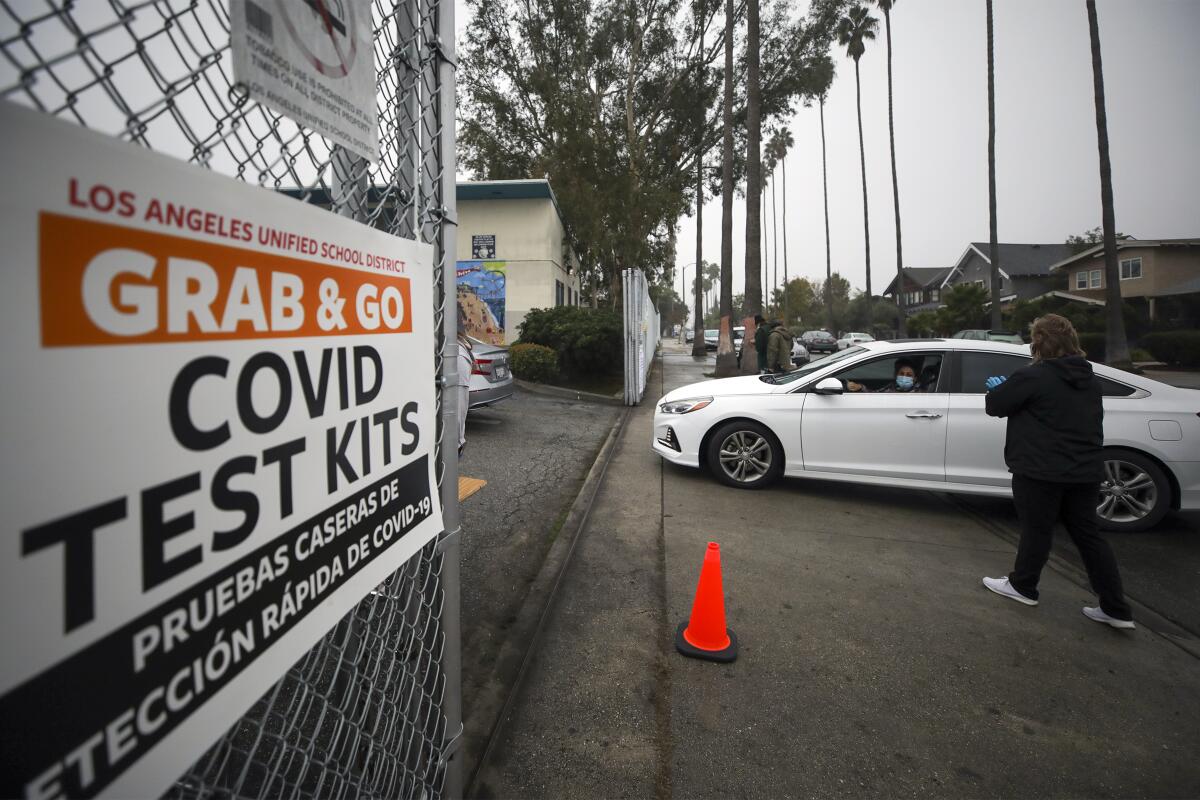 A car drives up to a sign that says "Grab and go COVID test kits"