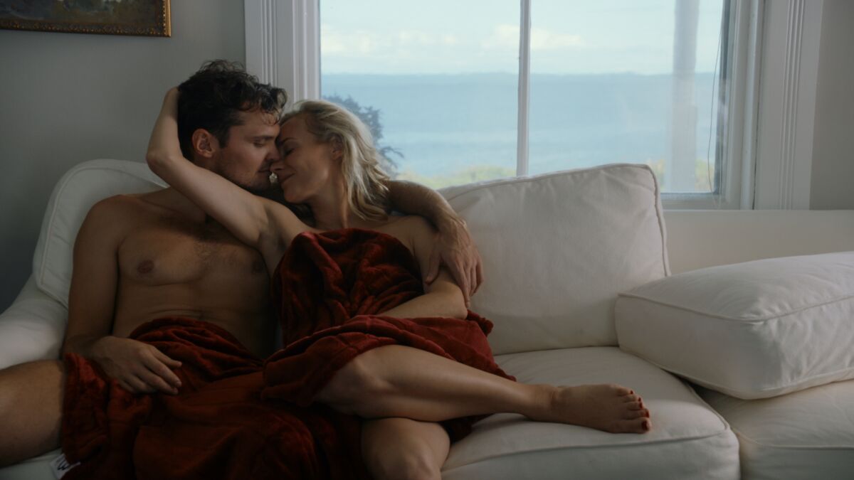 two people kiss on a couch with a window to the water behind them