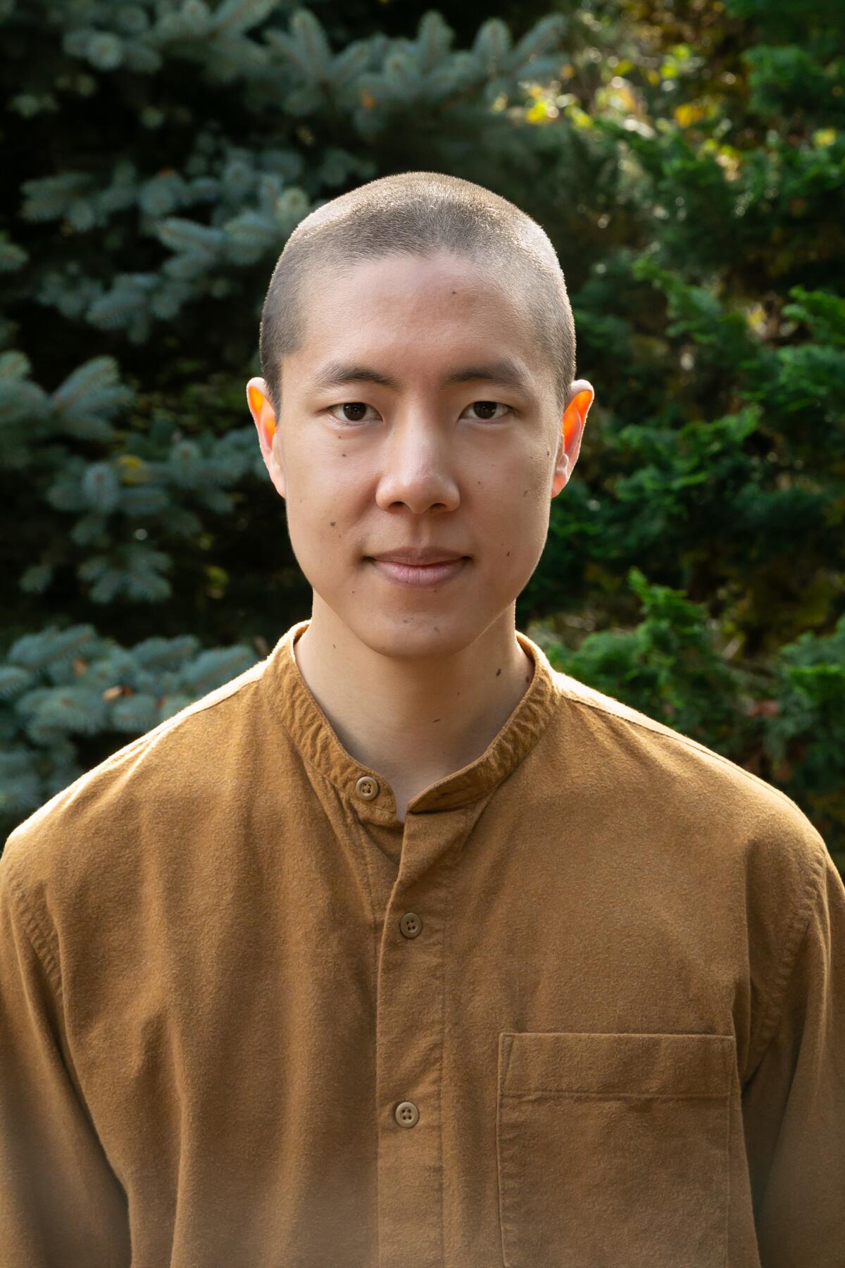 A man with a shaved head stands outside, smiling slightly and staring at the camera.