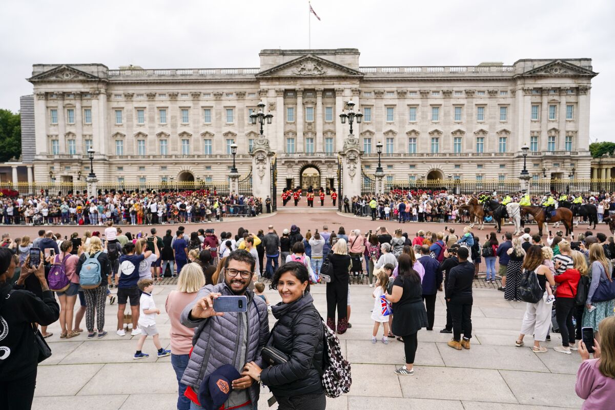 Two people take a selfie with Buckingham Palace in the background.