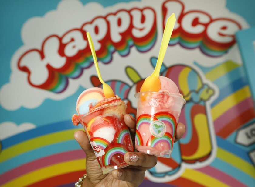 Closeup of a hand holding two plastic cups of ice cream in rainbow-covered plastic cups.