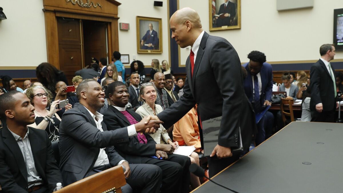 Sen. Cory Booker (D-N.J.), right, shakes hands with author Ta-Nehisi Coates in Washington as he waits to testify on June 19 about reparations for the descendants of slaves.