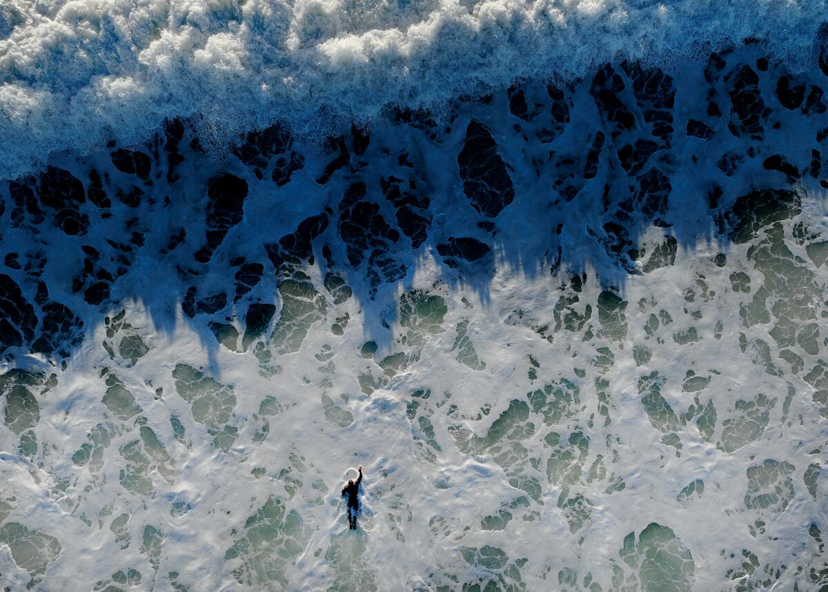 Aerial view of a surfer paddling out toward a wave in whitewater
