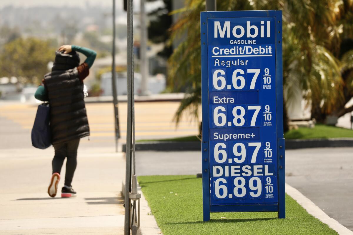 A pedestrian walks by a Mobil gas station with a sign showing gas prices topped $6 per gallon.