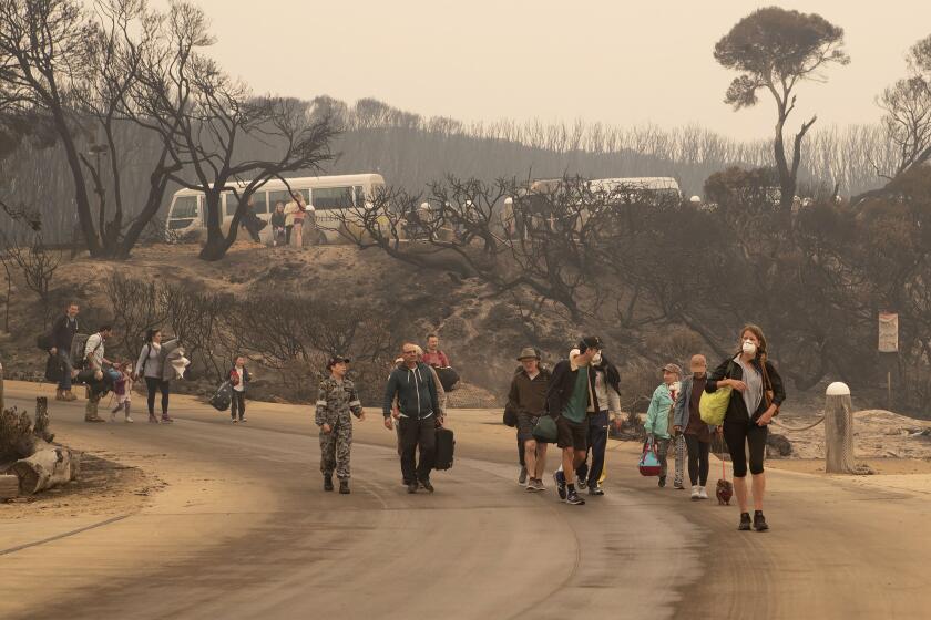 In this photo released by the Australian Department of Defense, evacuees walk down to the beach to board vessels and be ferried out to the navy's HMAS Choules, Friday, Jan. 3, 2020, in Mallacoota, Victoria, Australia. Navy ships plucked hundreds of people from beaches and tens of thousands were urged to flee before hot weather and strong winds in the forecast worsen Australia's already-devastating wildfires. (Australia Department of Defense via AP)