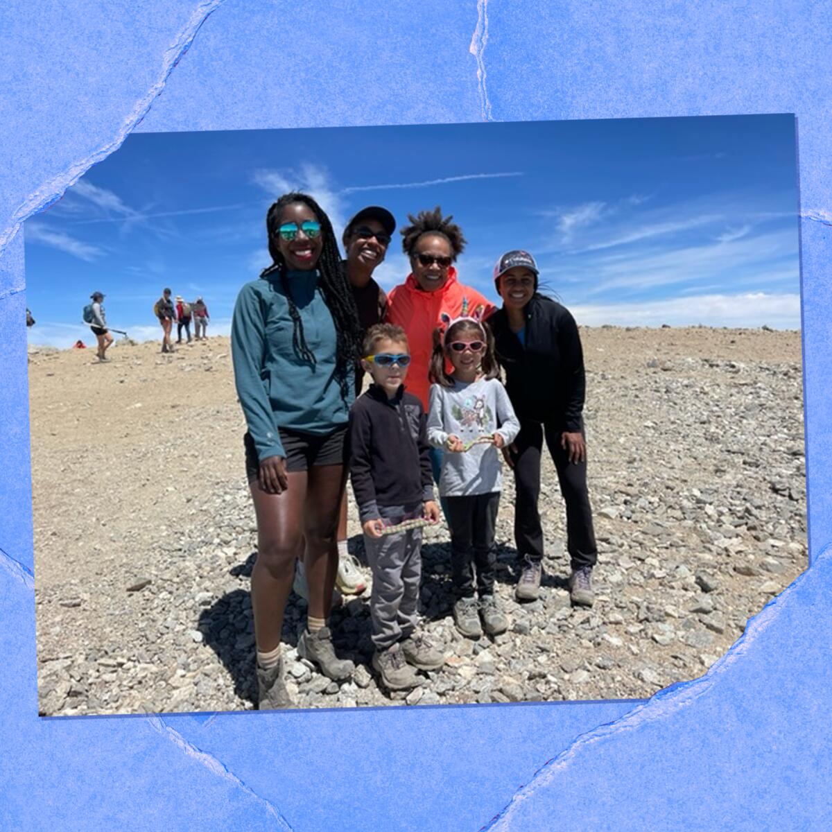 Six people, four older and two children, pose together for a photo on rocky ground.