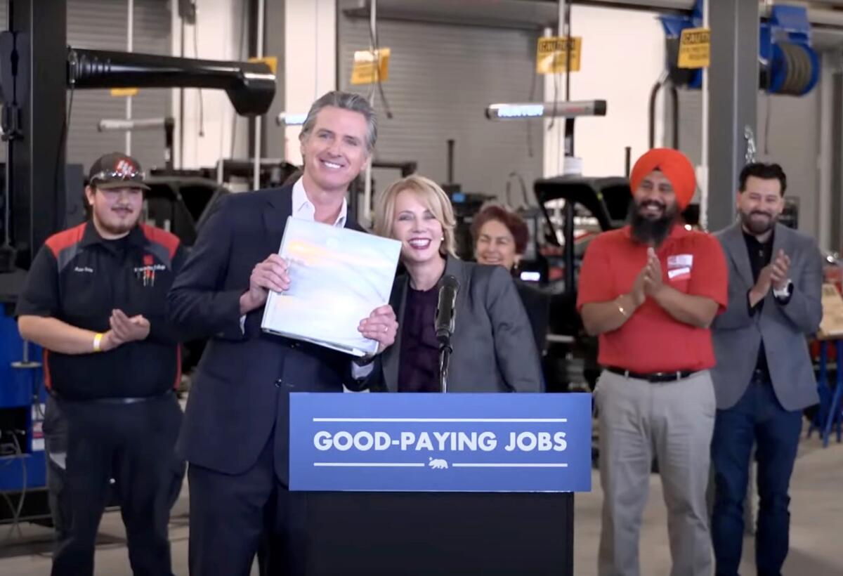 A man stands next to a woman at a lectern and holds up a sign or folder.