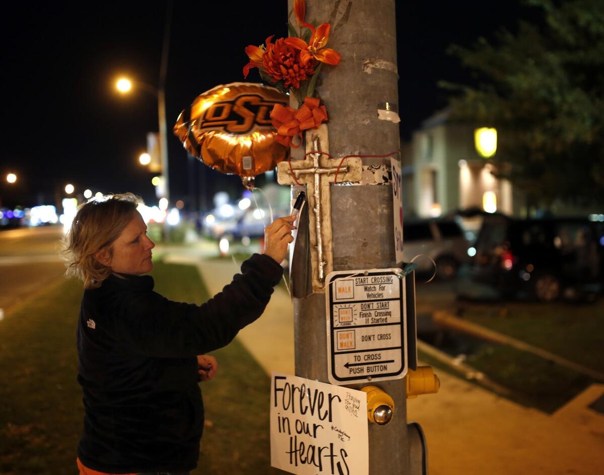 Teria Frank writes a message on a sign at a memorial in Stillwater, Okla., near where a car crashed into spectators during the Oklahoma State University homecoming parade.