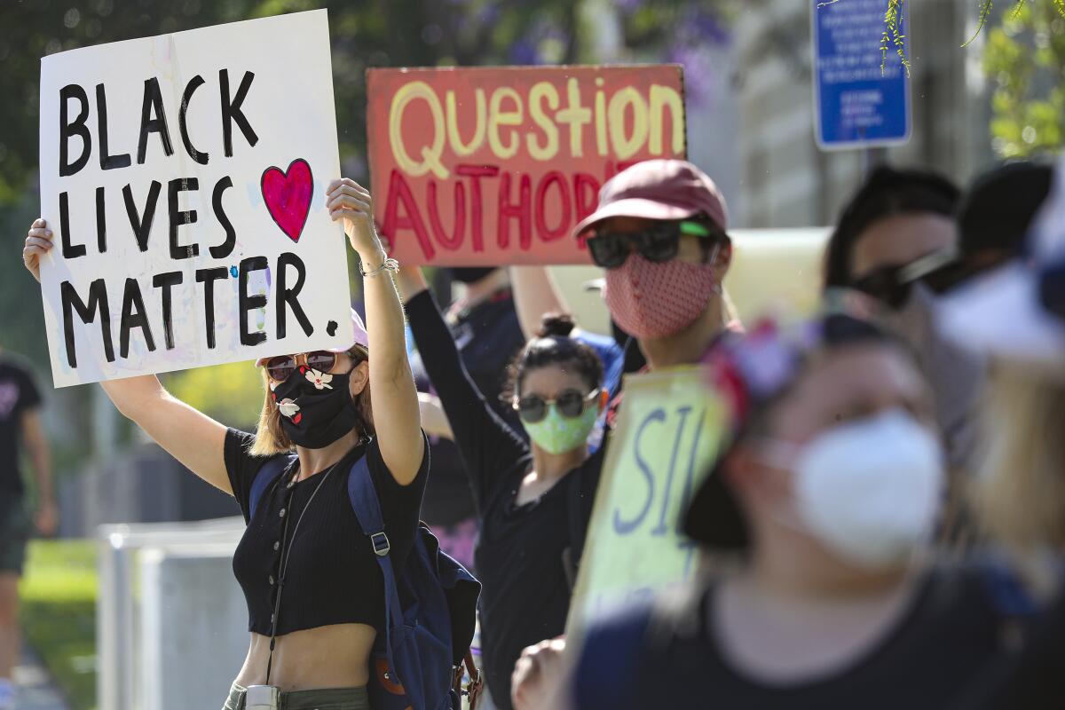 A woman raises a Black Lives Matter sign among a crowd of protesters outside the North Hollywood police station