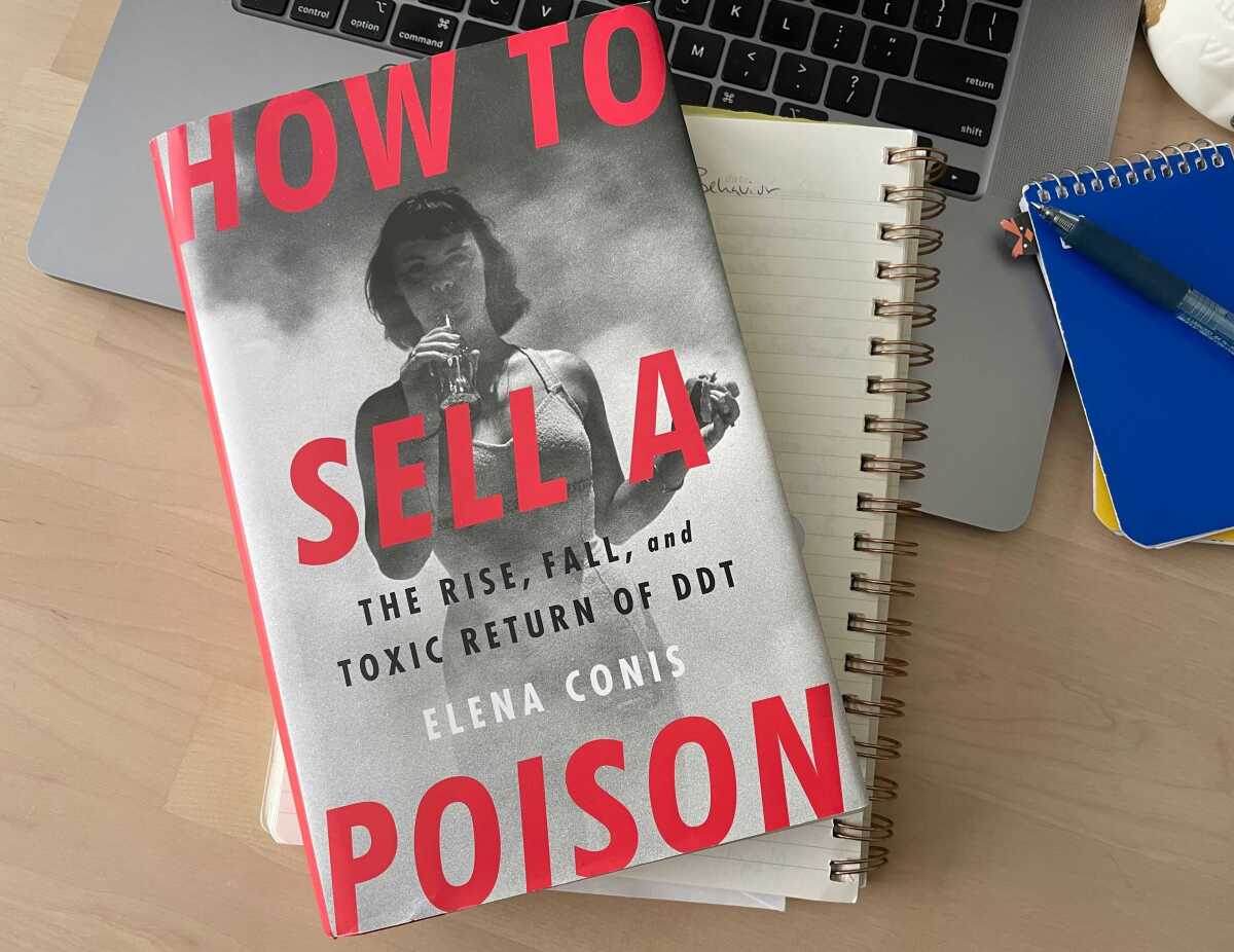 A book lies on top of a notebook and a laptop on a desk.