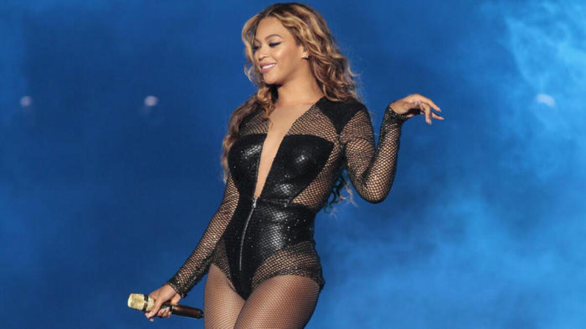 Beyoncé holds a microphone and smiles while wearing a black bodysuit