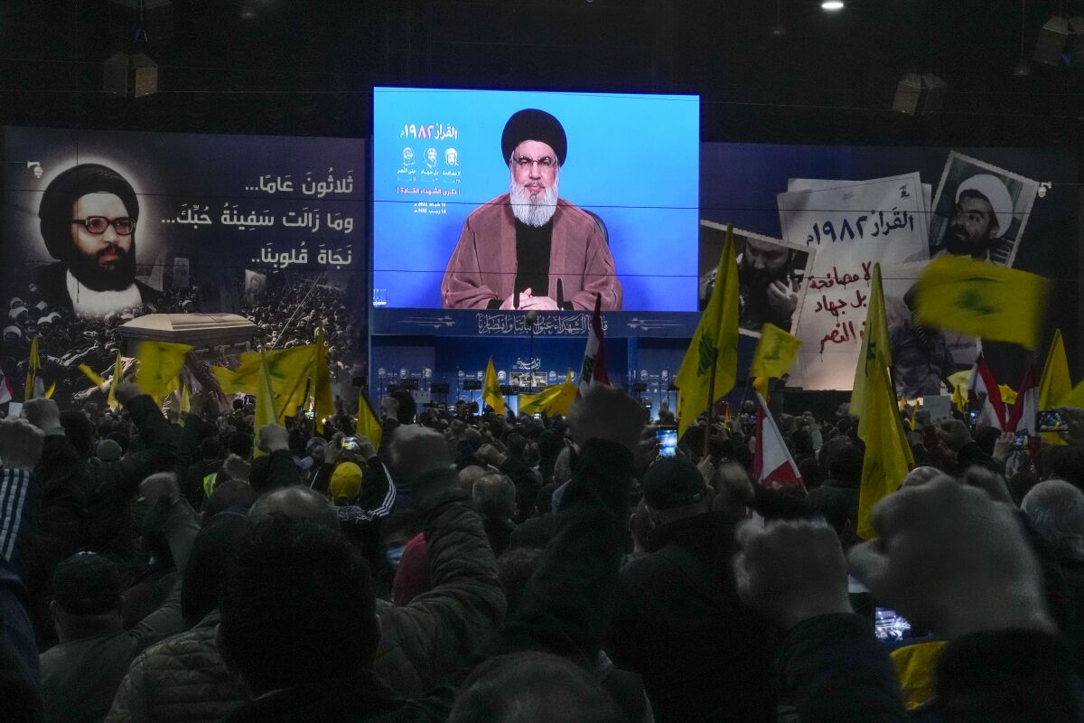 Hezbollah leader Sheik Hassan Nasrallah speaks via a video link as his supporters raise their hands, during an annual ceremony commemorating the killing of some of the Iran-backed group's top political and military leaders, in the southern suburb of Beirut, Lebanon, Wednesday, Feb. 16, 2022. Nasrallah revealed Wednesday in a televised speech that his militant faction has been manufacturing military drones in Lebanon and has the technology to turn thousands of missiles in their possession into precision-guided munitions. (AP Photo/Hassan Ammar)