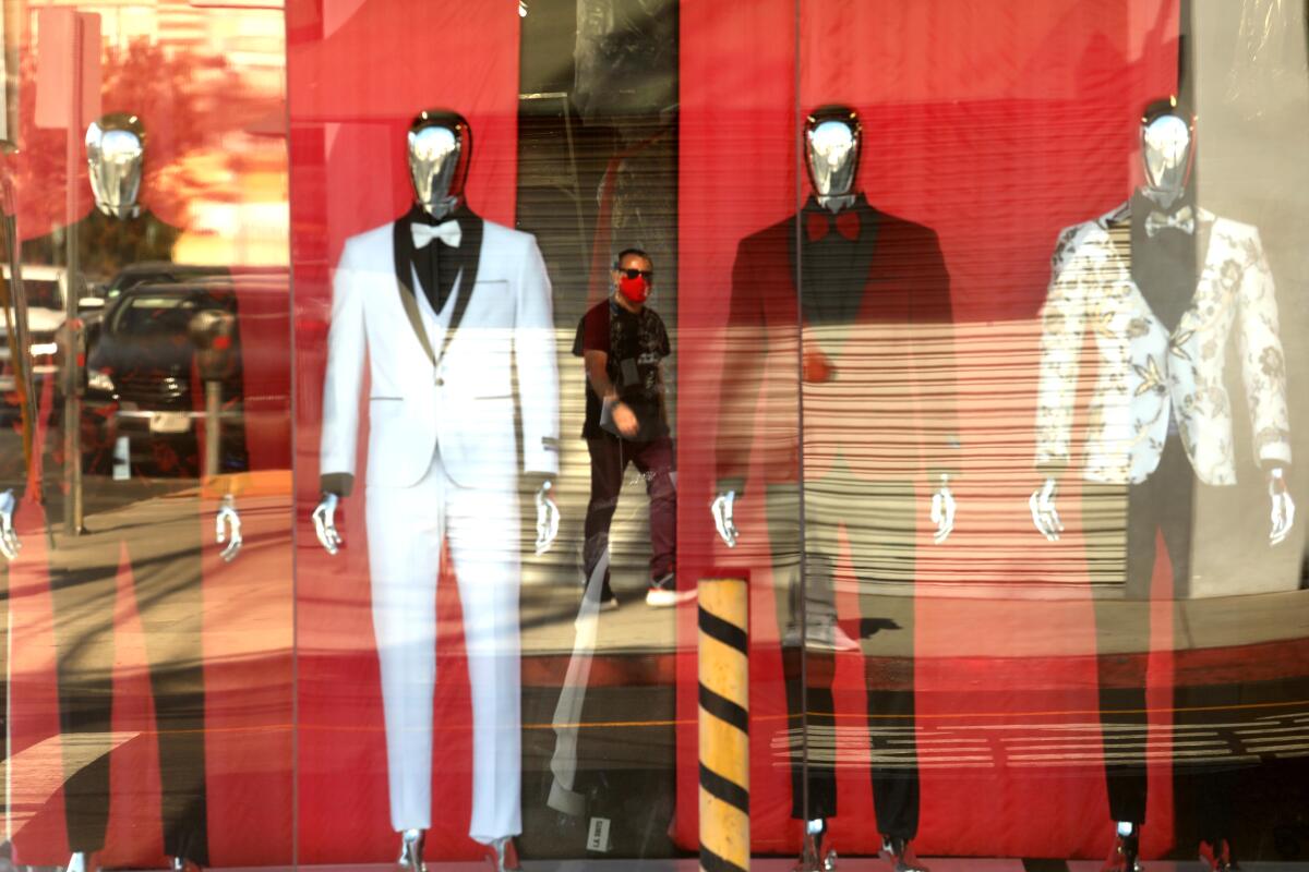 A pedestrian, wearing a mask, is reflected in the storefront of L.A. Suits along Maple Street in the Garment District.