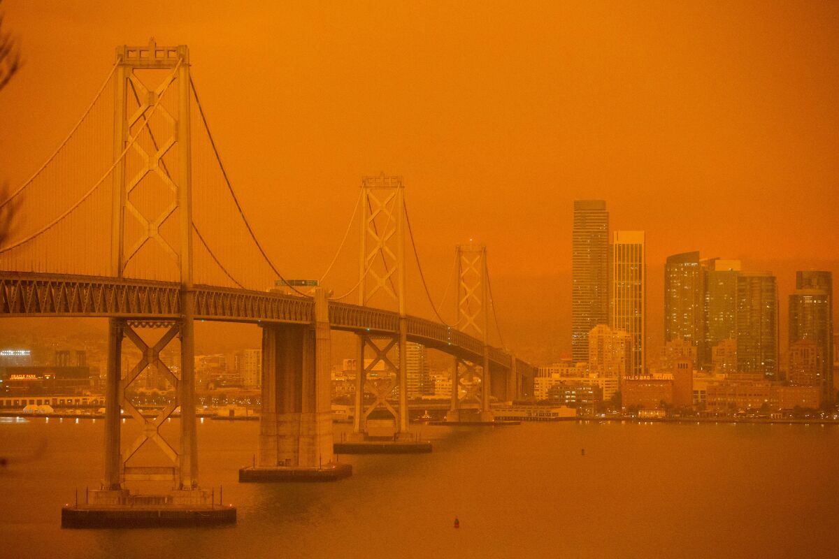 The San Francisco Bay Bridge and city skyline are obscured in orange smoke and haze.